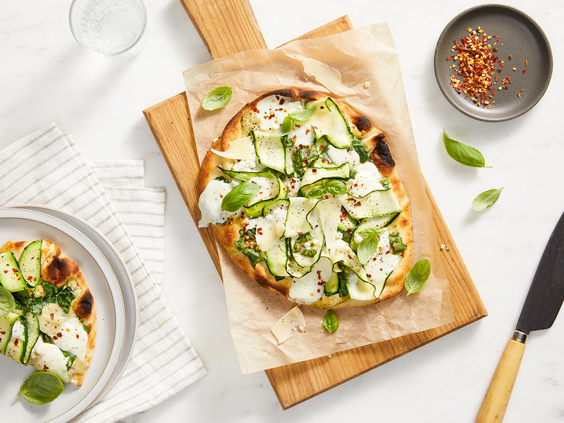 An image of prepared Creamy Pesto Flatbreads made with Prego® Creamy Roasted Garlic Pesto Sauce, spinach, naan, mozzarella, feta, zucchini and Parmesan.