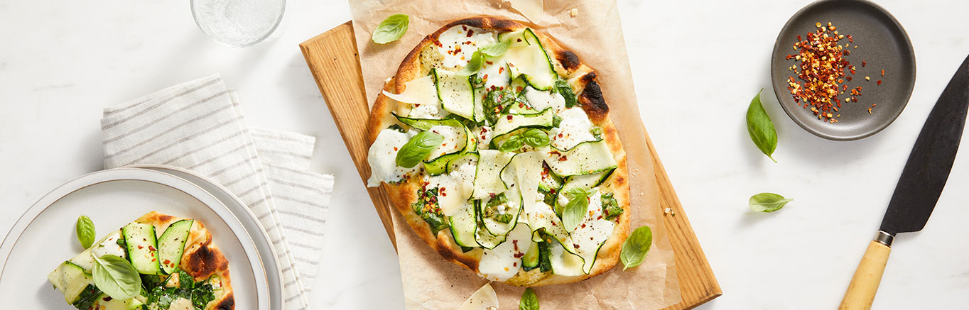 An image of prepared Creamy Pesto Flatbreads made with Prego® Creamy Roasted Garlic Pesto Sauce, spinach, naan, mozzarella, feta, zucchini and Parmesan.