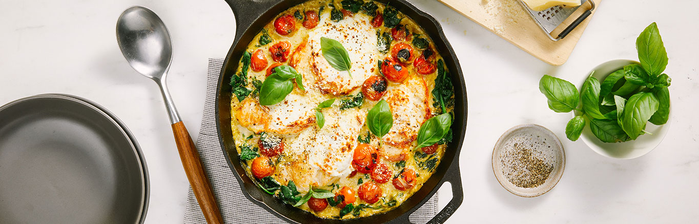 An image of prepared Skillet Creamy Pesto Chicken Caprese made with chicken, tomatoes, Prego® Creamy Parmesan Pesto Sauce, spinach, mozzarella and Parmesan cheese.
